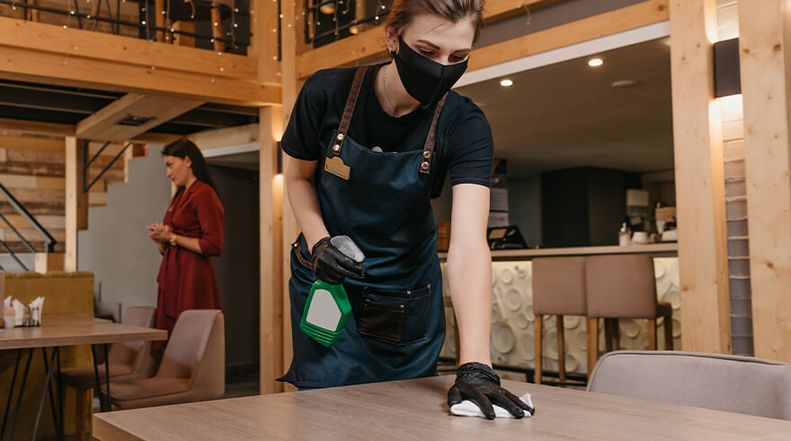 Restaurant woman employee disinfecting tables as per recommended safety measures.